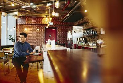 Man looking away sitting in a restaurant smiling with laptop.